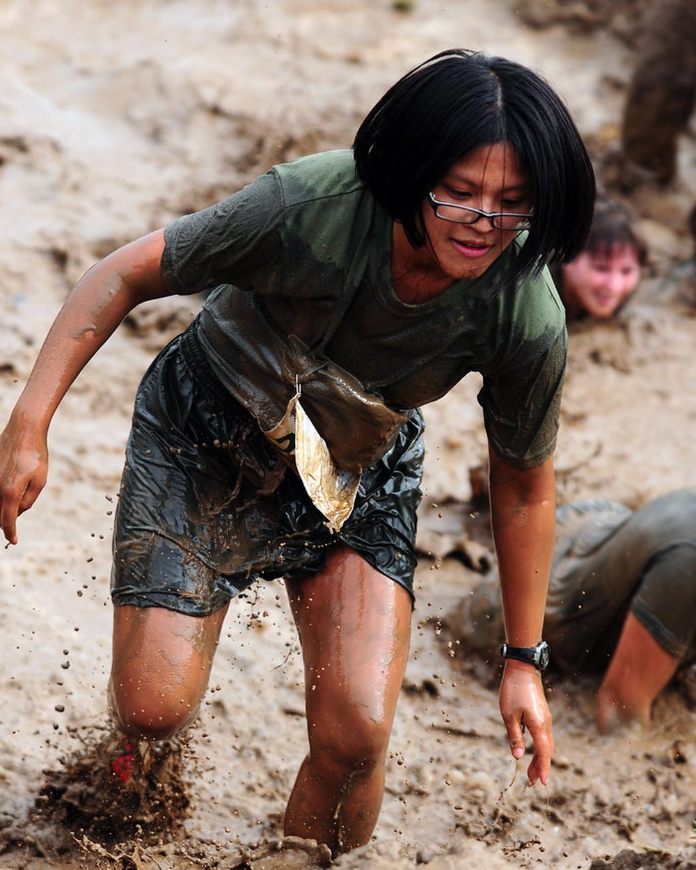Athlete pushing hard through a gruelling mud obstacle course, soaked and driven — the BENSCHIZO grit of turning an unconventional mind into relentless training.